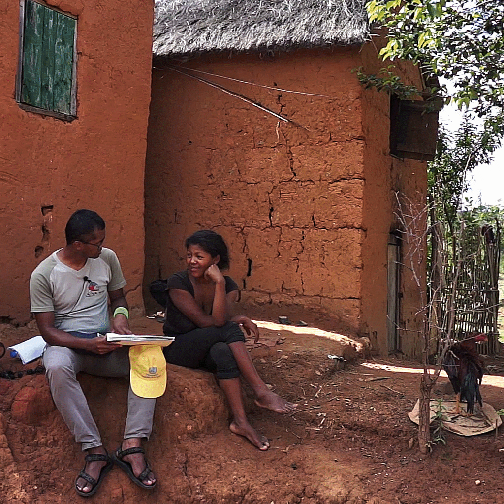 An interview setting in a participant’s front yard, in the community of Behenjy, Madagascar. The translator is showing the food group collages to the participant, to survey the dietary diversity score of her child. A typical brick house of the highland region is also shown in the photo.